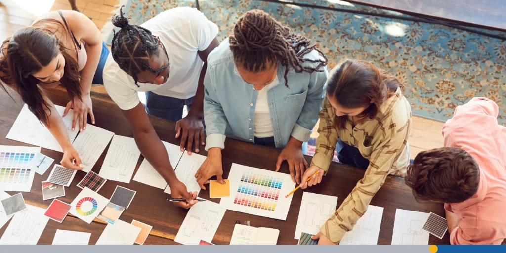 Overhead View Of Team Having Creative Design Meeting Around Wooden Table In Office