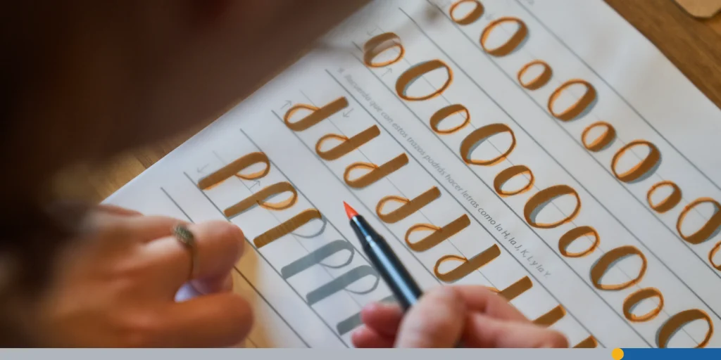 Crop person practicing lettering using orange felt pen