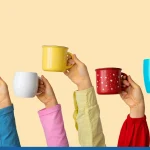 Many different hands holding multi colored cups of coffee on a pastel background