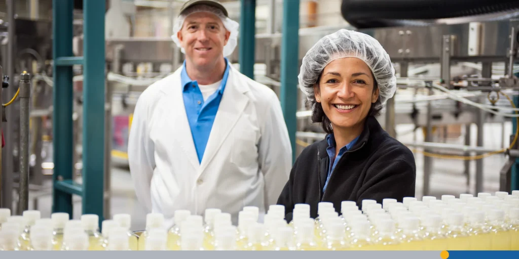Workers wearing head nets and standing near a conveyor belt of bottles in a bottling plant