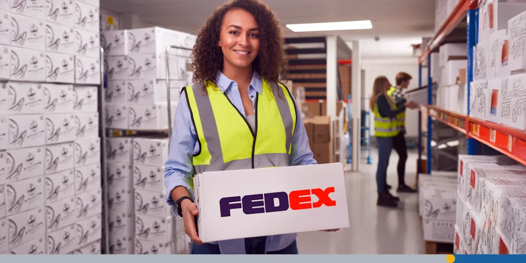 Portrait Of Female Worker Inside Busy Warehouse Carrying Box 