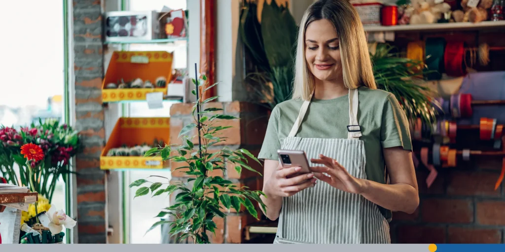 Woman florist using a smartphone while working in a flower shop