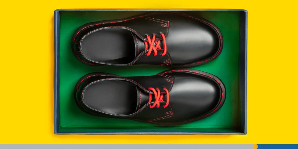 Stylish black leather shoes in a box on yellow background