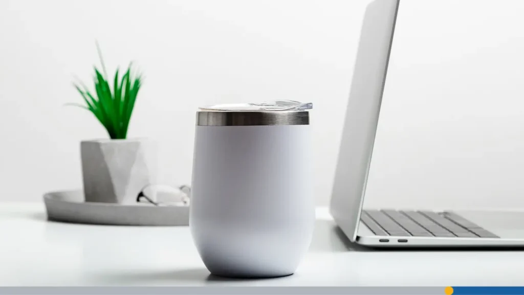 White travel coffee mug next to a computer