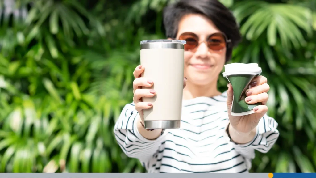 Woman holding up a reusable mug and a crumpled up paper cup