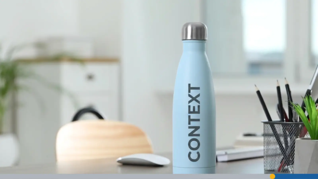 A tumbler with a lid sits on an office desk, featuring the word context printed across it, representing branded office supplies.