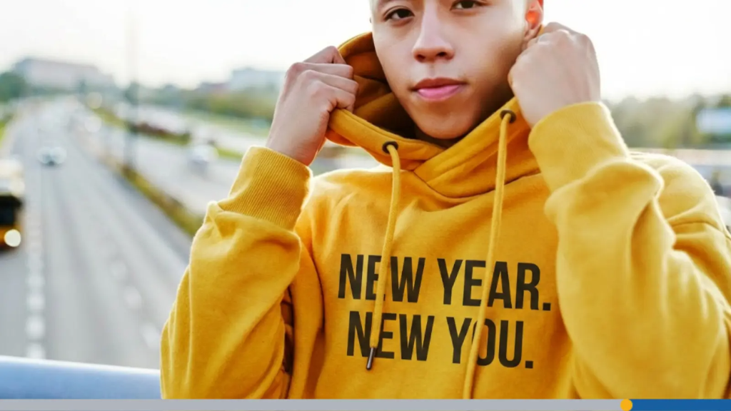 A young man wears a hoodie with the words new year, new you sewn into it, representing corporate gift ideas.