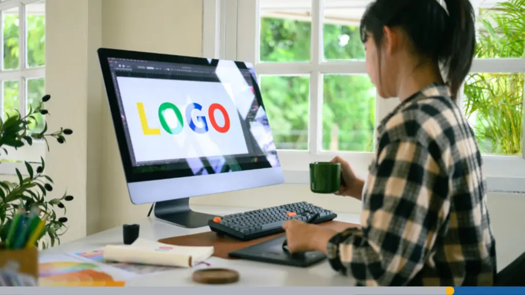 An office worker sits at a computer to create a brand online by designing a large logo on the screen.