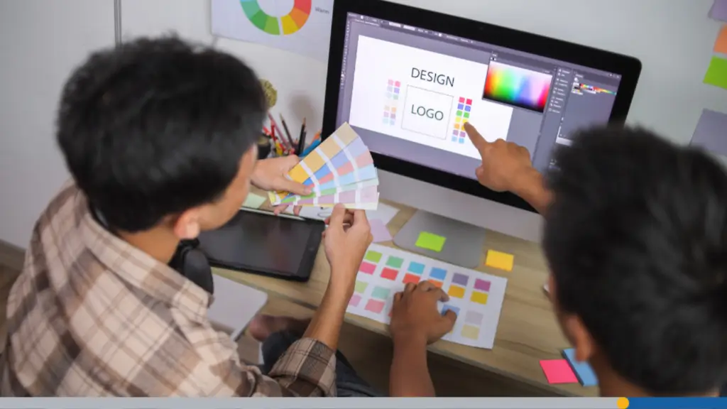 Two young men collaborating at a desktop computer to design a logo and order business cards online.