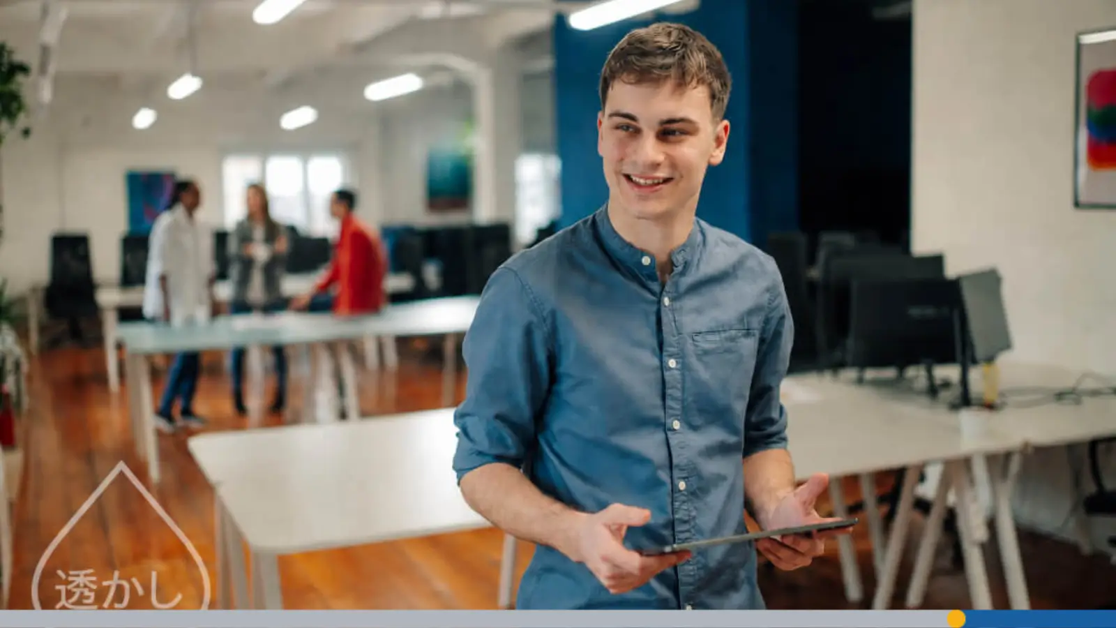 A smiling young man holding a tablet in a modern open-plan office, representing a guide to YouTube image dimensions.