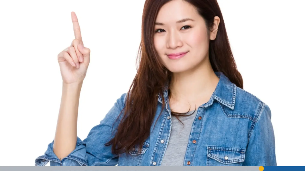 A woman in a denim shirt pointing her index finger upward with a friendly expression, highlighting helpful business name tips.