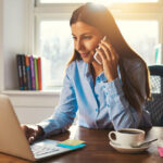 woman sitting at her desk on her phone looking at laptop