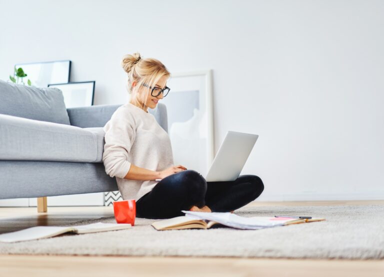 female looking at laptop searching for logo designs sitting on the floor of apartment