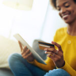 Woman looking at tablet with credit card in hand paying for item