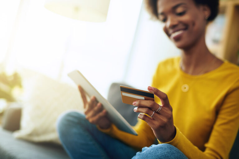 Woman looking at tablet with credit card in hand paying for item