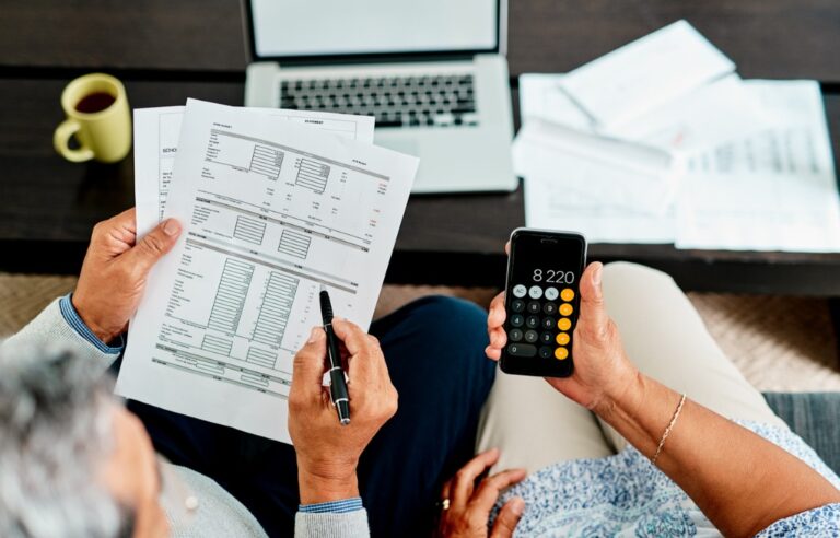 Two people reviewing a spreadsheet and usins a phone calculator